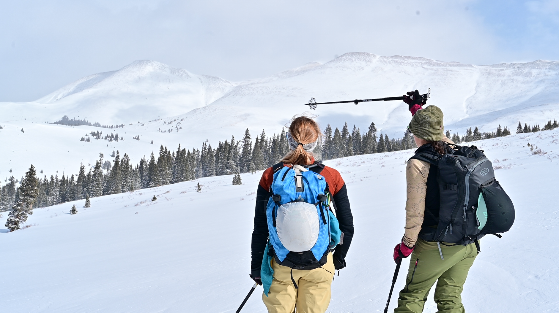 Two backcountry skiers pausing to take in a snow-covered mountain landscape, with one pointing toward the peaks ahead.